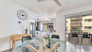 A modern kitchen with stainless steel appliances, a dining area with a glass table and chairs, and a view of the outside balcony. - Darwin Inner City Oasis | 2 Bed Apt (Darwin City)