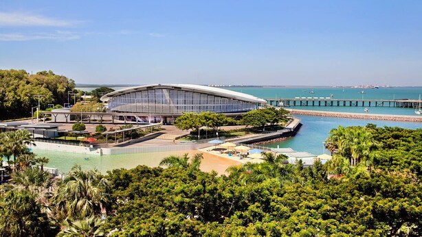 A modern stadium with a curved roof, surrounded by lush greenery and a waterfront. - Darwin Inner City Oasis | 2 Bed Apt (Darwin City)