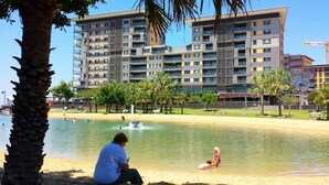 A waterfront park with a fountain, palm trees, and a building with multiple balconies in the background. - Waterfront Pearl Suite: 2 Bed Luxury Apt by Tropical BNB (Darwin City)