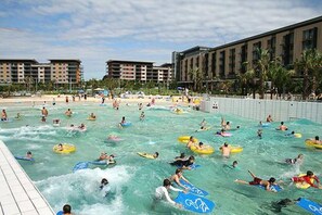 A water park with multiple swimming pools, people on water slides, and a large building in the background.