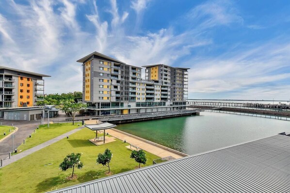 A modern apartment complex with multiple buildings, a waterfront view, and a pedestrian bridge.