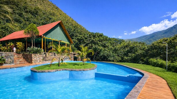 A swimming pool with a wooden deck, a building with a red roof, and lush greenery in the background. - www.ecoterralodge.com (Santa Teresa)