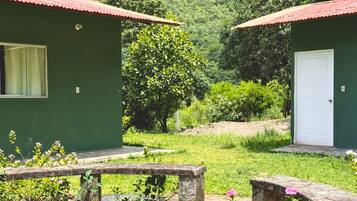 Dos edificios verdes con techos rojos, un hogar de piedra y flores rosadas en un jardín.