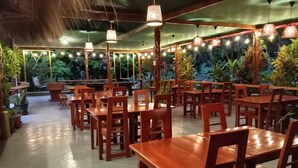 An indoor dining area with wooden tables and chairs, hanging pendant lights, and potted plants. - www.ecoterralodge.com (Santa Teresa)