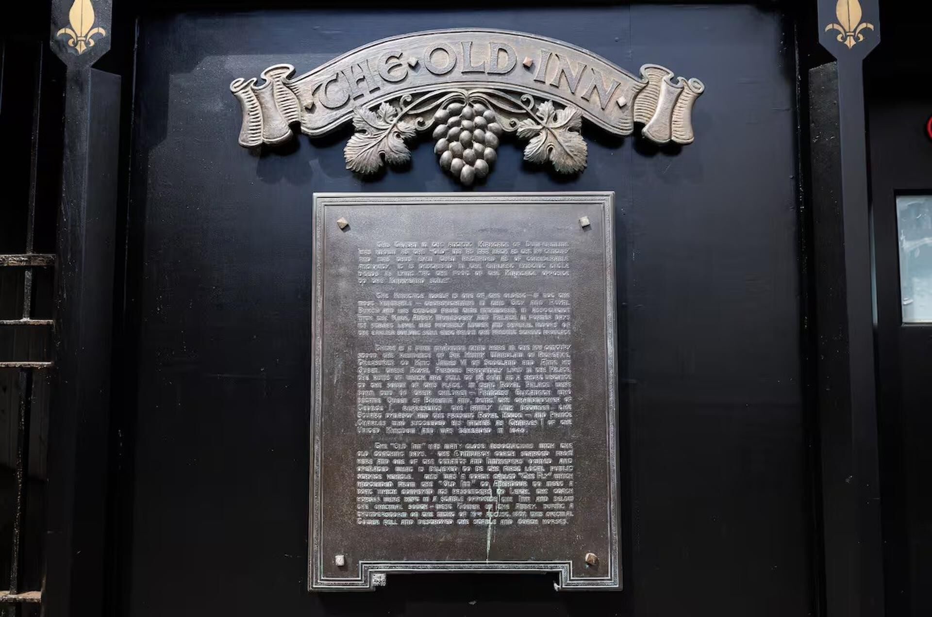 A plaque with the text "CHEOOLD INN" and decorative elements like grapevines and fleur-de-lis.