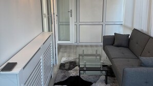 A modern living room with a glass coffee table, grey sofa, and a patterned rug.