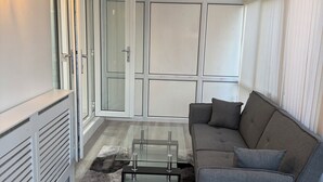A modern living room with a glass coffee table, grey sofa, and a fluffy rug.