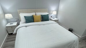 A modern bedroom with a large bed, two bedside tables with lamps, and a neutral color scheme.