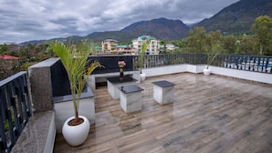 A rooftop terrace with a wooden floor, seating area, and potted plants. - Kailasham Stay (Dharamshala)