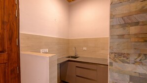 A compact kitchen with a built-in sink, a wooden door, and a stone backsplash. - Kailasham Stay (Dharamshala)