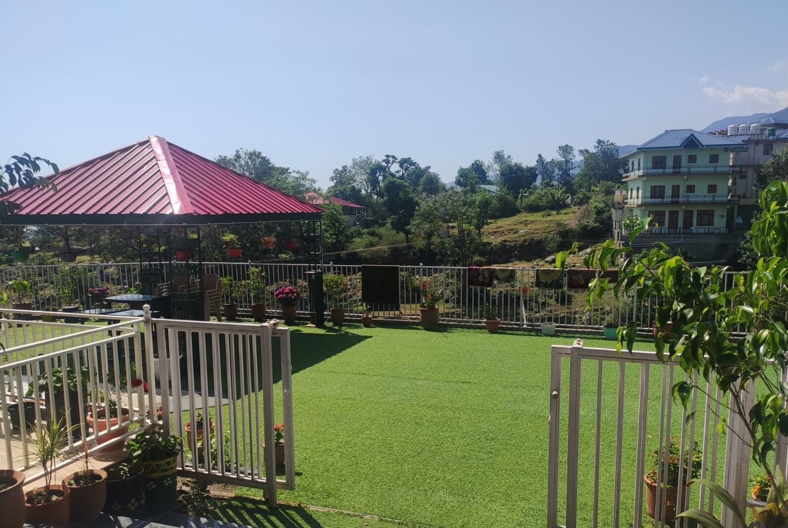 Un jardín trasero cercado con césped artificial, plantas en macetas y un pabellón.