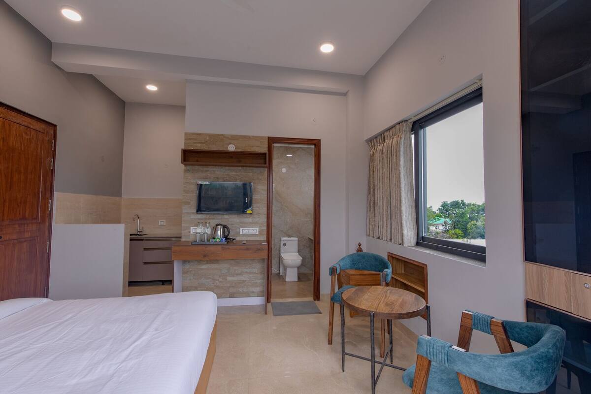 A hotel room with a bed, a small kitchenette, a bathroom, and a seating area with a table and chairs.