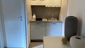 Eine kleine Küche mit weißen Schränken, einer Spüle und einer Arbeitsplatte. Eine Tür führt in einen anderen Raum, und ein Tisch steht mit zwei Vasen darauf.