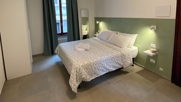 Ein Schlafzimmer mit Bett, Nachttisch, Spiegel und einem Fenster mit Vorhängen.