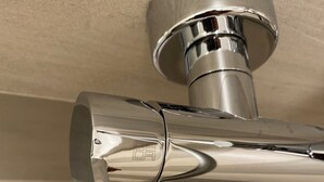 Ein chromfarbener Wasserhahn mit Hebelgriff, an einer beige gestrichenen Wand befestigt.
