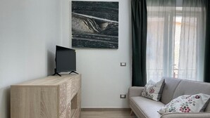 A modern living room with a wooden console table, a flat-screen TV, a grey sofa with floral cushions, and a large abstract painting on the wall. - Greta family house: Clare (Roma)
