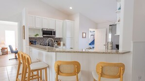 Una cocina moderna con armarios blancos, encimera de granito y tres taburetes de madera.