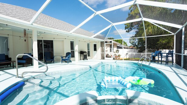 Una piscina con cerramiento de vidrio, sillas azules y un jacuzzi.
