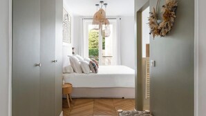 A bedroom with a bed, a window, a hanging light fixture, and a wall decoration. - ELEGANT APARTMENT IN THE HEART OF PARIS – STEPS FROM JARDIN DU LUXEMBOURG (Paris)