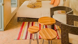 Een hotelkamer met een bed, twee houten krukken, een tafeltje, een radiator en een wandlamp.