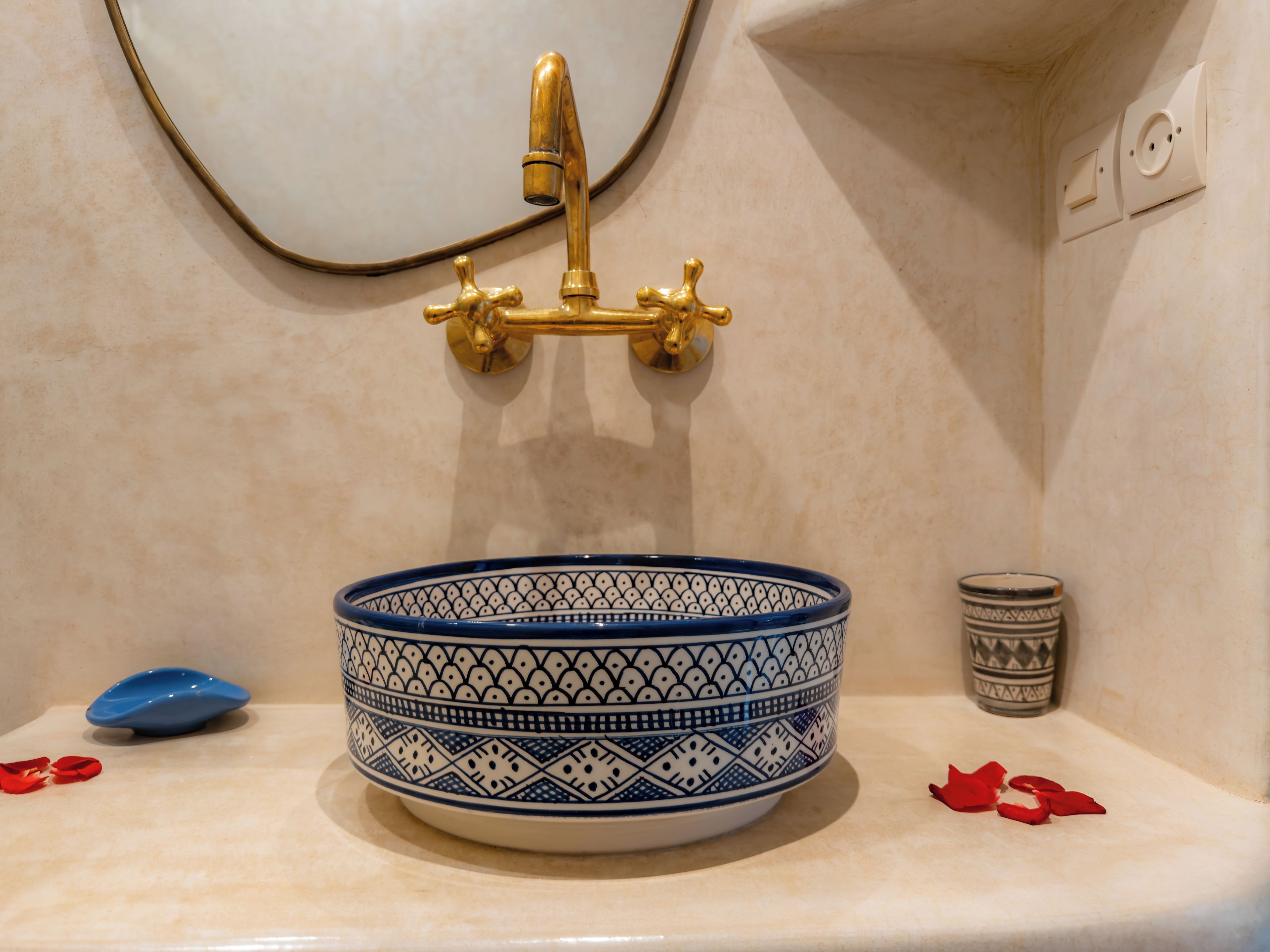A bathroom sink with a blue and white patterned basin, a gold faucet, and a mirror above it.