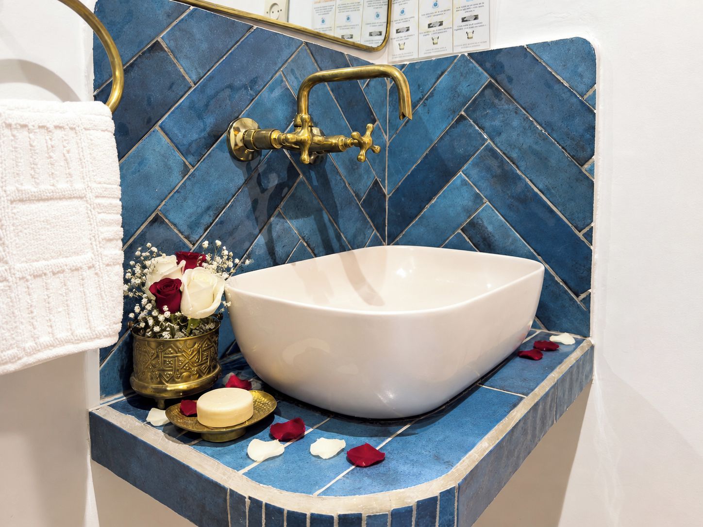 A bathroom with a white vessel sink, a gold faucet, and a blue tiled backsplash.