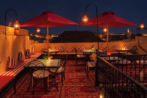 An outdoor dining area with tables and chairs, red umbrellas, and lanterns. - Riad Medina d'Or (Marrakech)