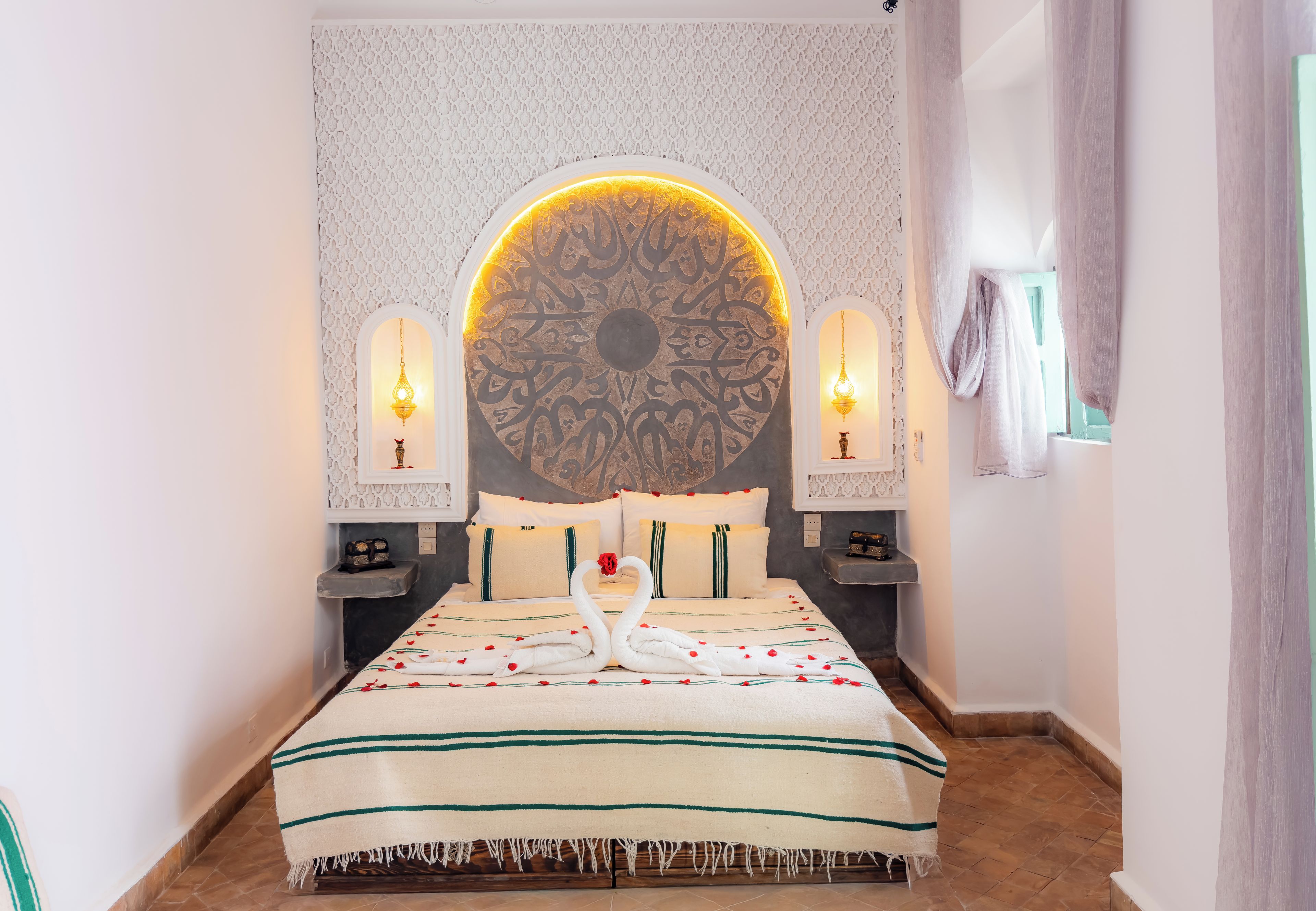 A hotel room with a large decorative wall, a bed with a floral bedspread, and two wall-mounted lamps.