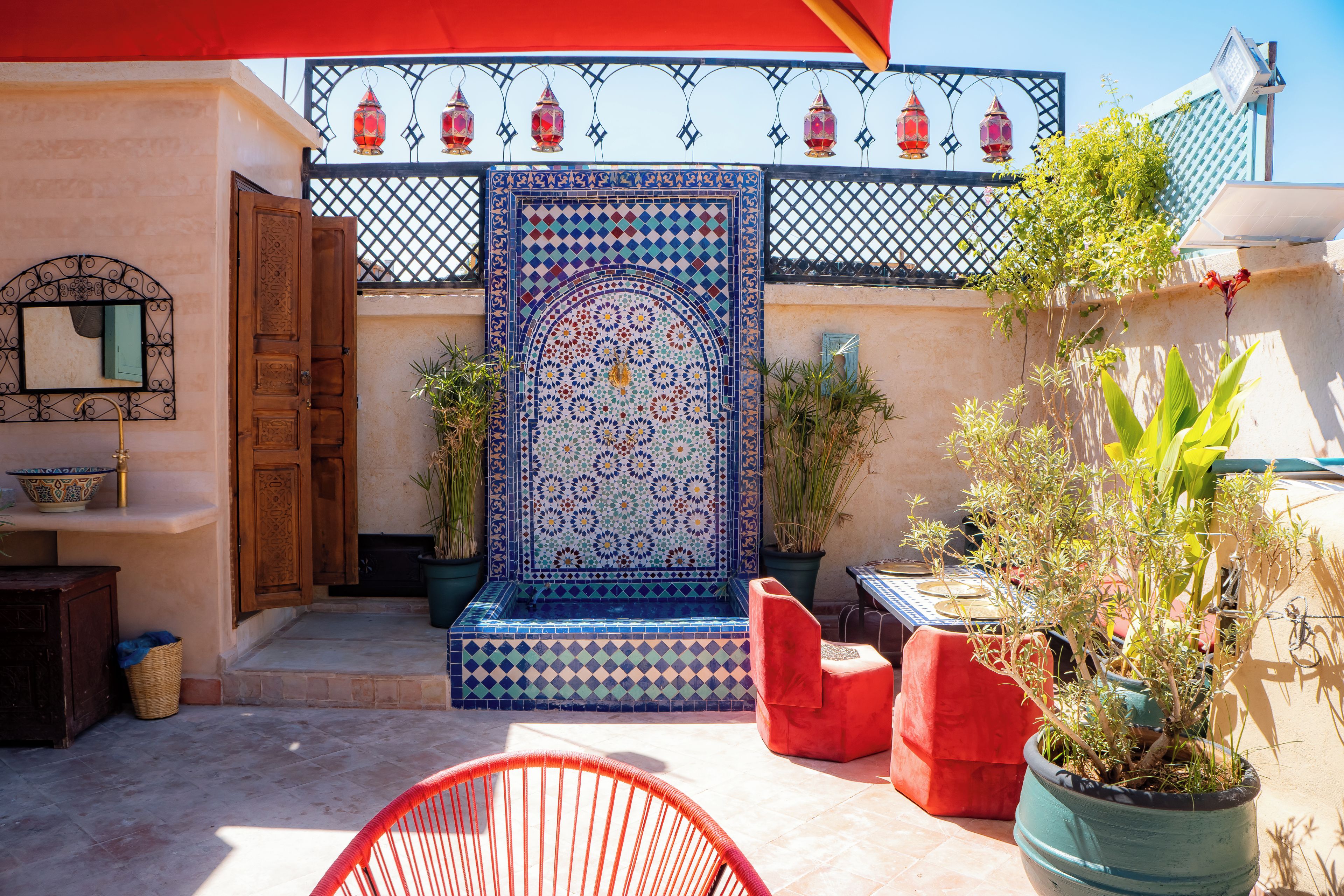 Un patio con un muro de azulejos, una puerta de madera y una silla roja.