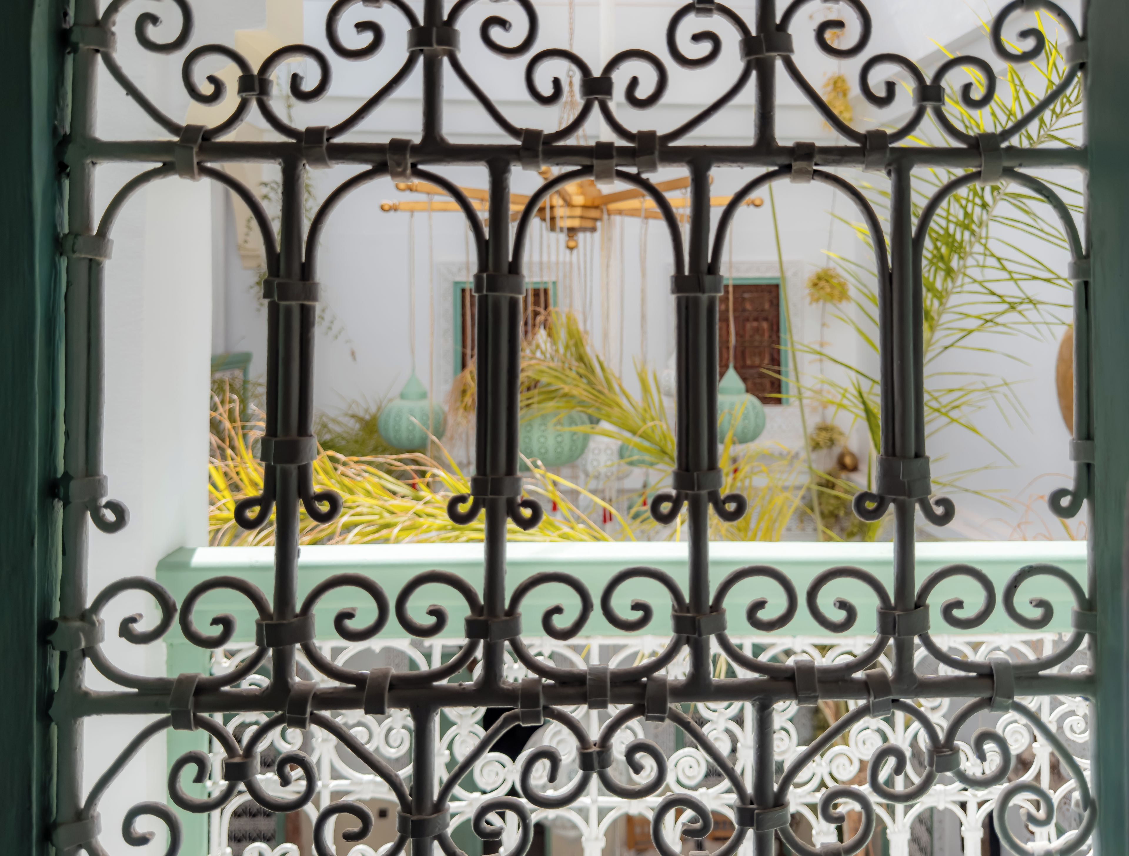 A wrought iron gate with intricate designs, leading to a room with a green wall and a window.