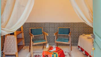 Una habitación con dos sillas de madera, una mesa pequeña con un mantel colorido y una pared con estampado.