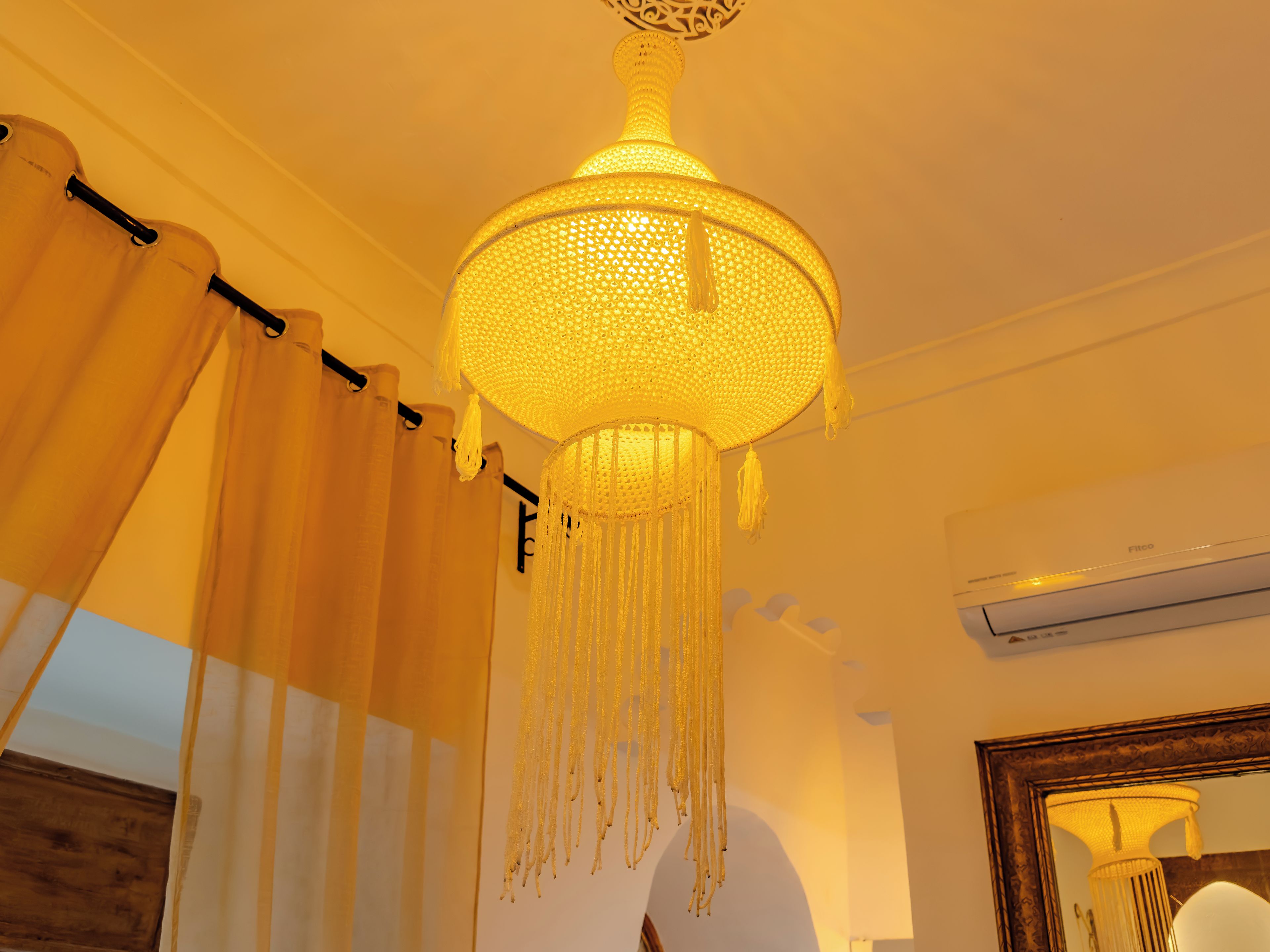 Une pièce avec un lustre suspendu, des rideaux, un appareil de climatisation et un miroir.