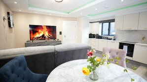 A modern living room with a fireplace, grey sofa, and a dining table with a vase of flowers. - Charming London House - Sleeps 4 & Outdoor Space (London)