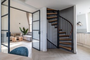Un intérieur moderne avec un escalier en colimaçon, un coin salon agrémenté d’une plante et un espace cuisine.