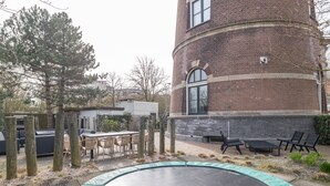 Un bâtiment en briques doté d’une fenêtre circulaire, d’un espace extérieur aménagé pour s’asseoir et d’un trampoline.