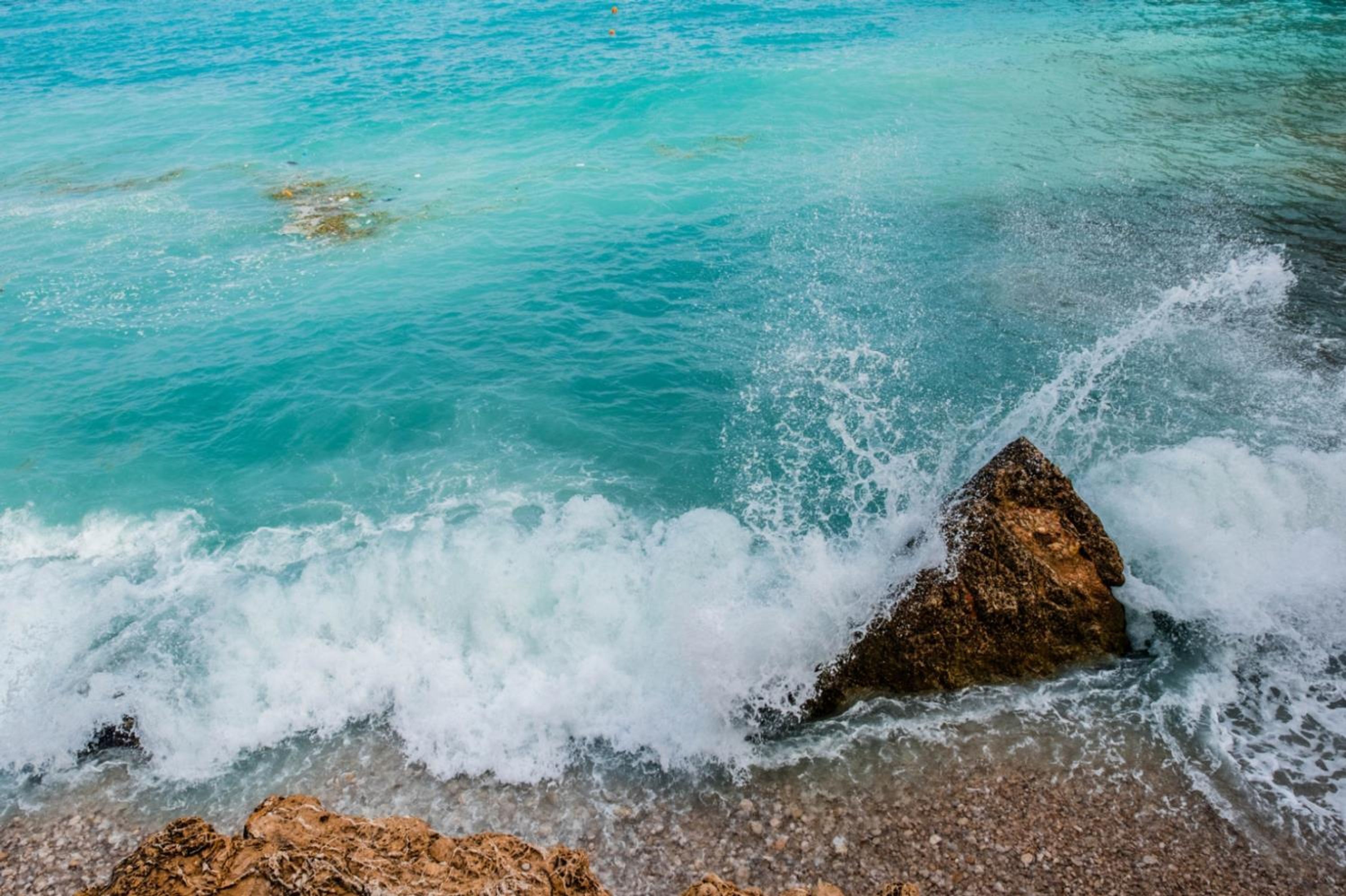 A rocky shoreline with clear turquoise water and waves crashing against the rocks.