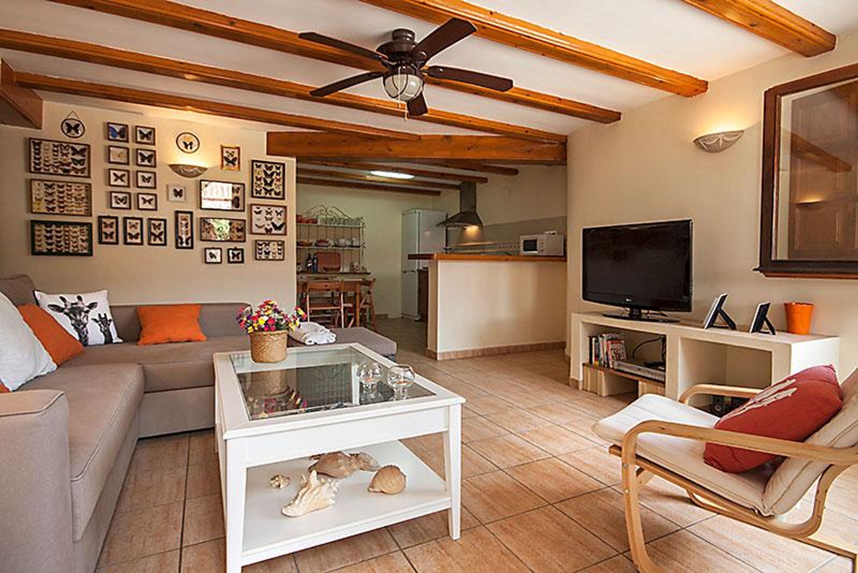 A living room with a sofa, coffee table, and armchair, a television, and a kitchen area in the background.