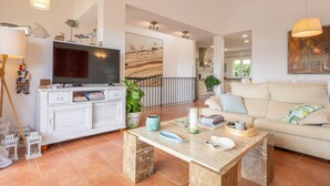 Un salon spacieux avec une télévision, des meubles blancs, une table basse et un canapé beige.