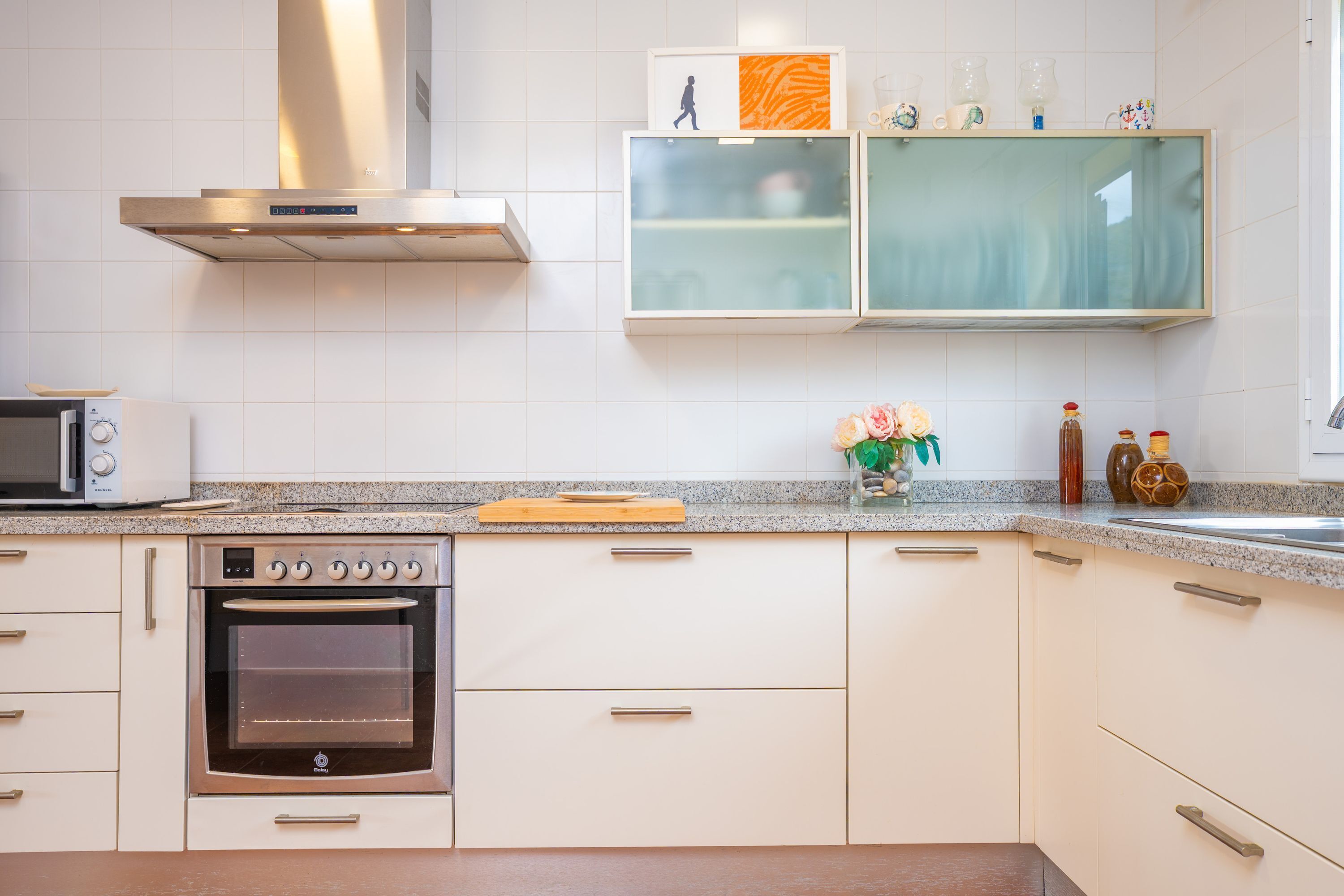 Une cuisine avec des armoires blanches, un four encastré, un four à micro-ondes et une hotte de cuisinière en acier inoxydable.