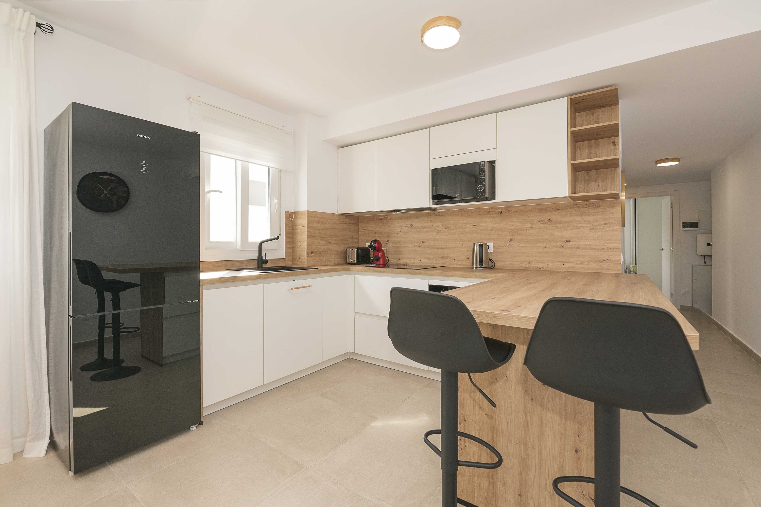 A modern kitchen with white cabinets, a black refrigerator, a microwave, and two black bar stools.