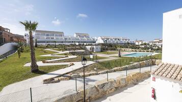 Zona residencial con edificios blancos modernos, una piscina y un jardín bien cuidado con palmeras.