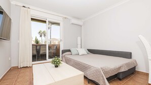 A modern bedroom with a bed, a small table, and a sliding glass door leading to a balcony. - Novo Golf Chiclana in Chiclana de la Frontera (Chiclana de la Frontera)