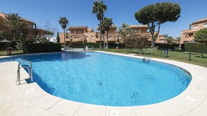 A swimming pool with a metal ladder, surrounded by a concrete deck. There are palm trees and a hedge in the background. - Novo Golf Chiclana in Chiclana de la Frontera (Chiclana de la Frontera)