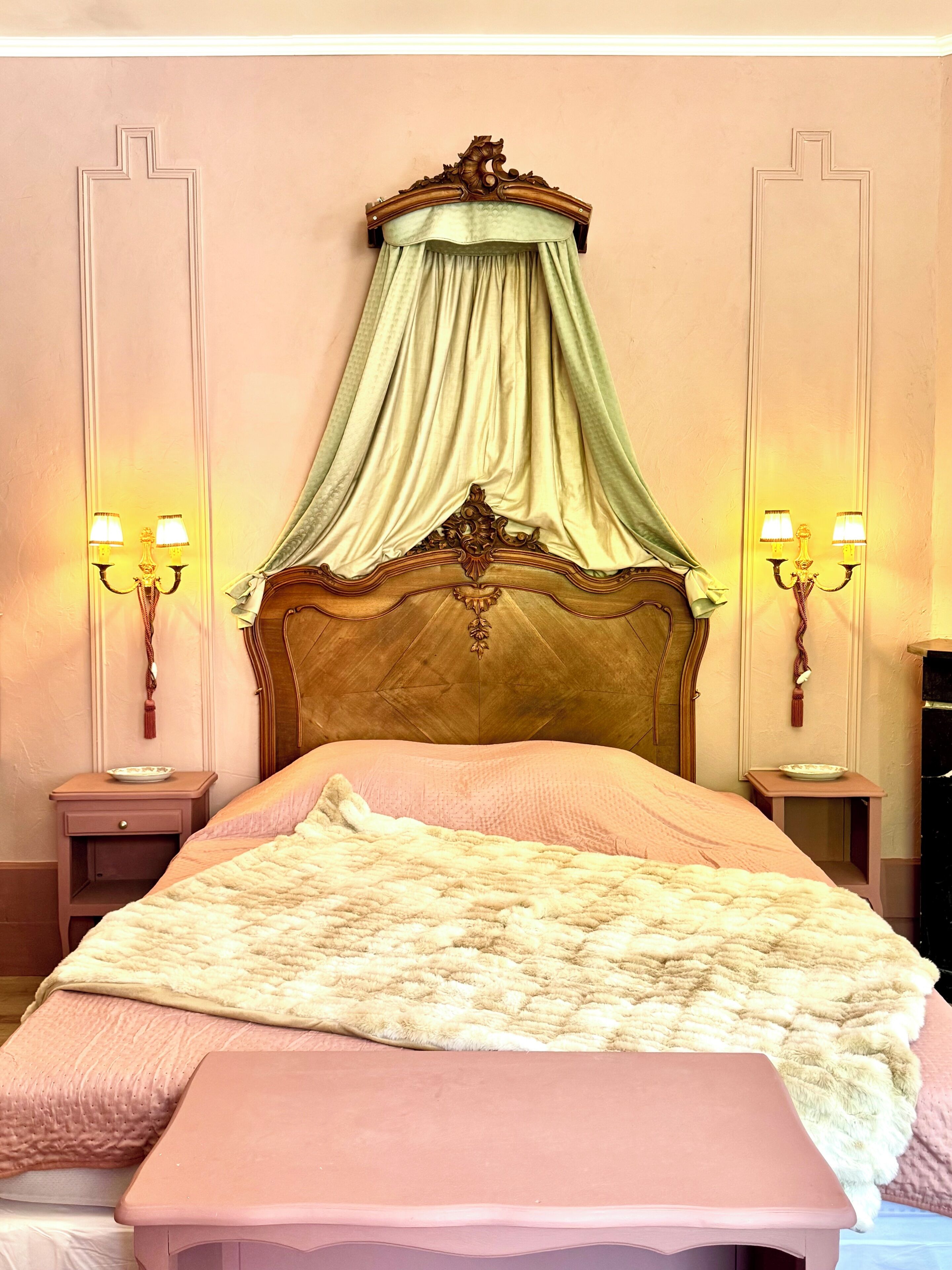 Ein Schlafzimmer mit einem Himmelbett, einem Baldachin, zwei Nachttischen mit Lampen und einer Bank am Fußende des Bettes.