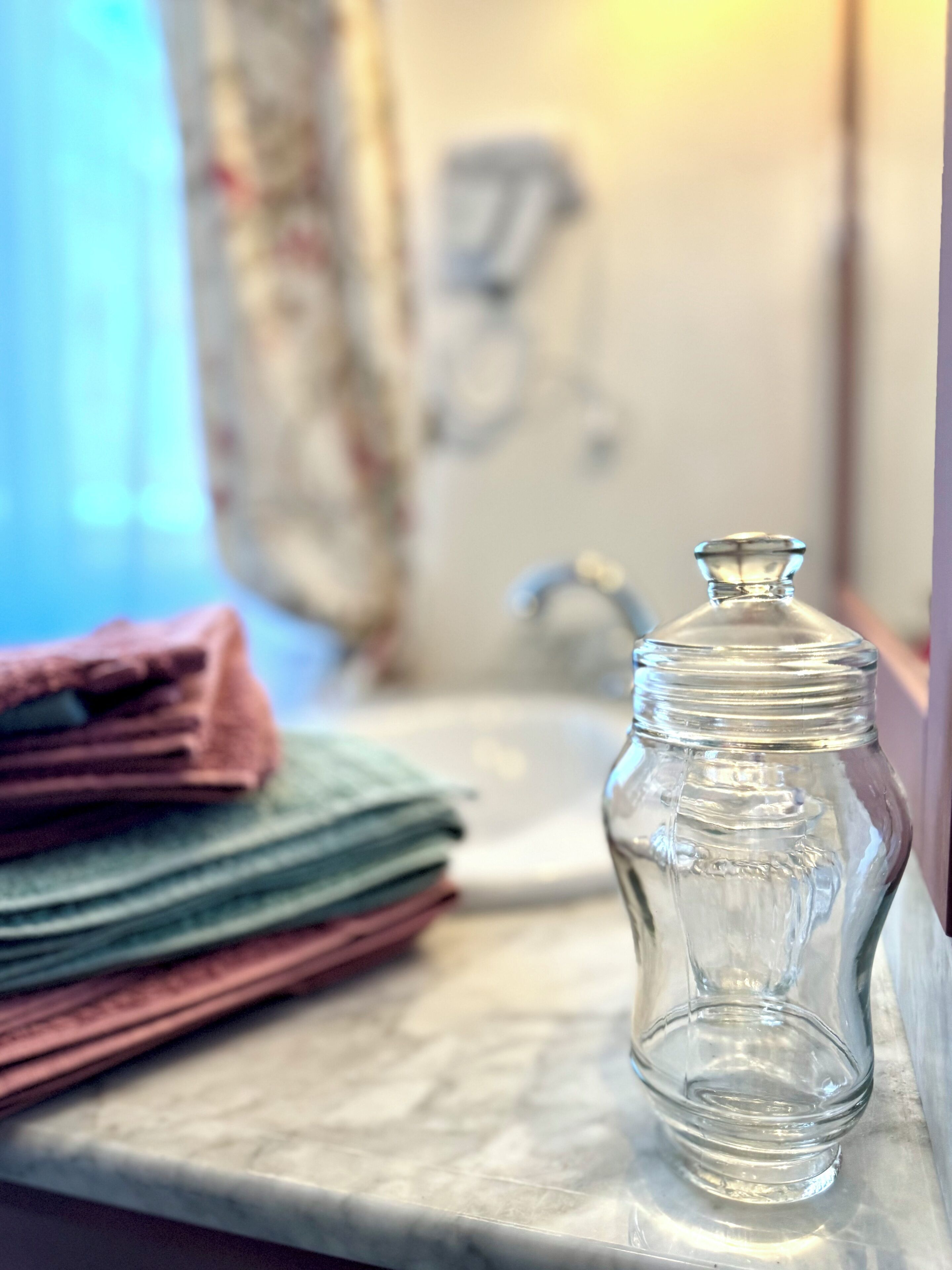 A clear glass jar on a marble countertop with a stack of folded towels in the background.