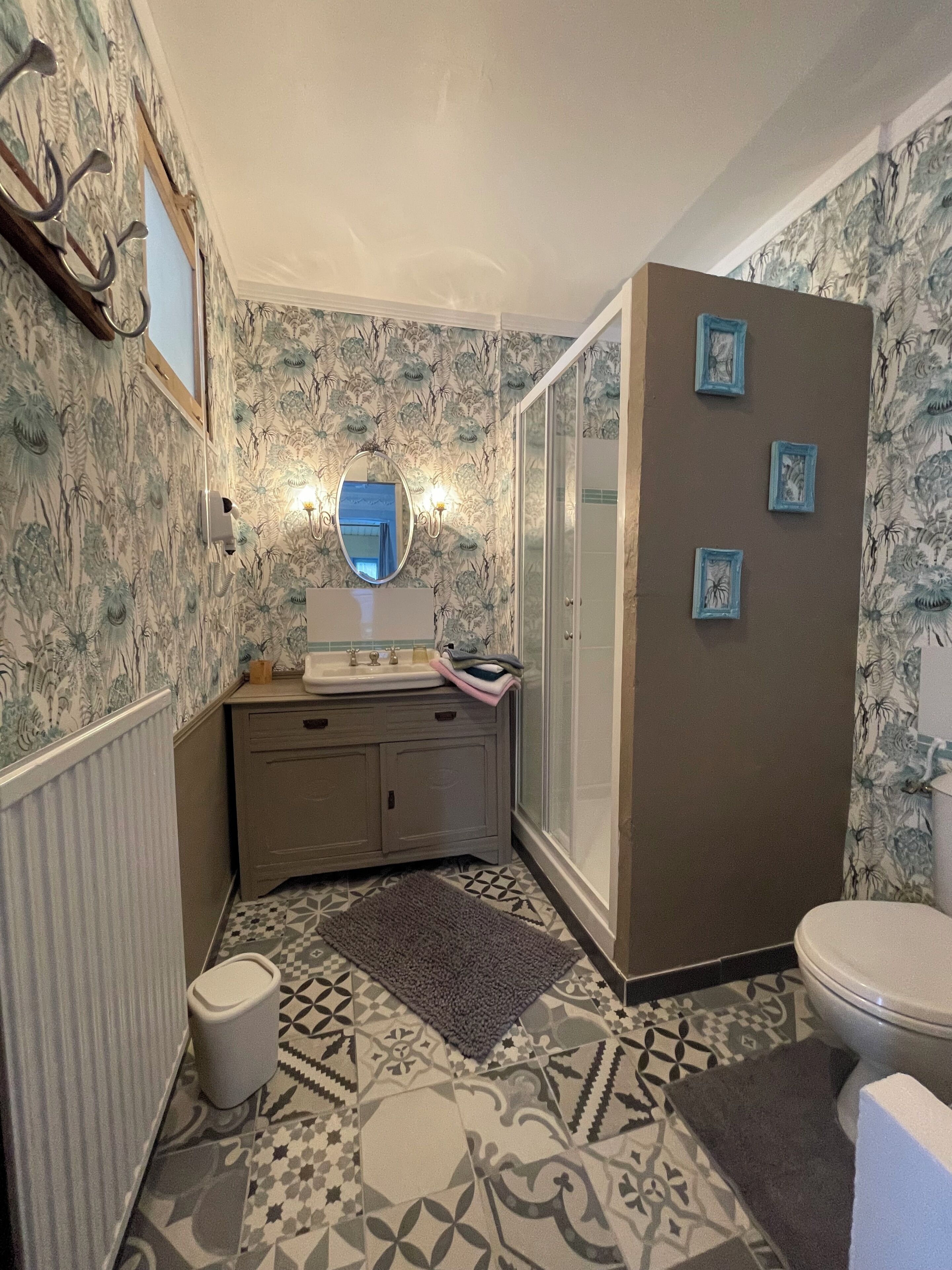 Een badkamer met een vloer met een patroon, een wastafel met spiegel, een toilet en een douchegedeelte.