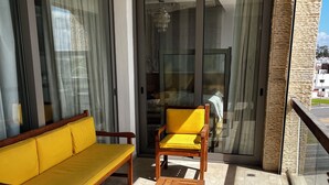Un balcon avec un canapé jaune, des chaises en bois et une table en bois.