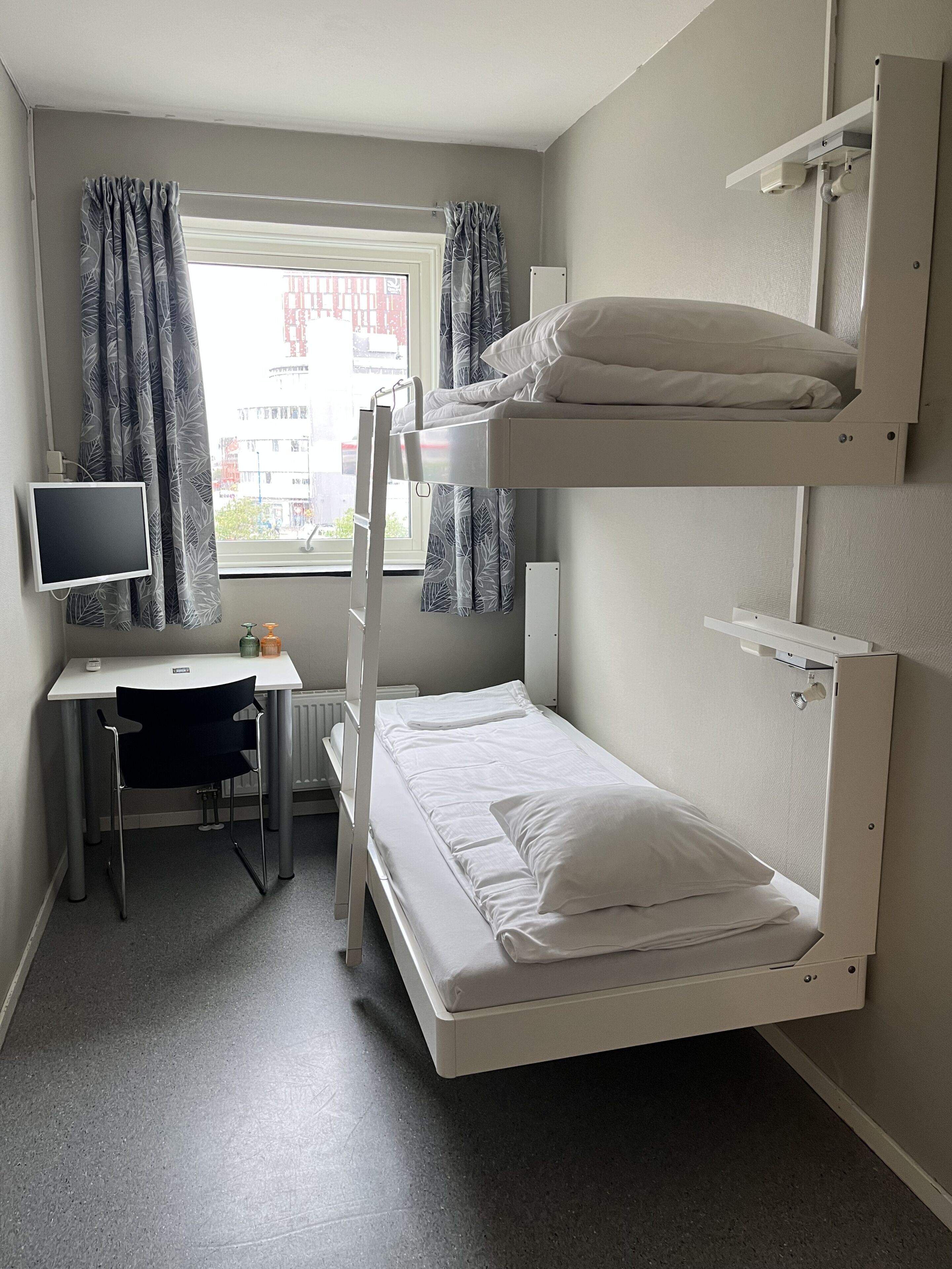 Une chambre avec un lit superposé, un bureau, une chaise et une fenêtre avec des rideaux.