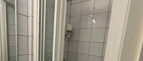 Un baño con mampara de vidrio, lavamanos blanco y paredes con azulejos.