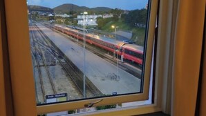 A window view of a train station with multiple tracks and a red train in motion. - Bodo Motel Norway (Bodø)